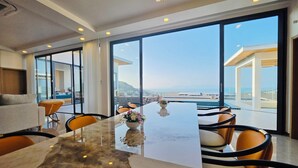 Un comedor moderno con una mesa de mármol, sillas color naranja y grandes ventanales con vistas al mar.