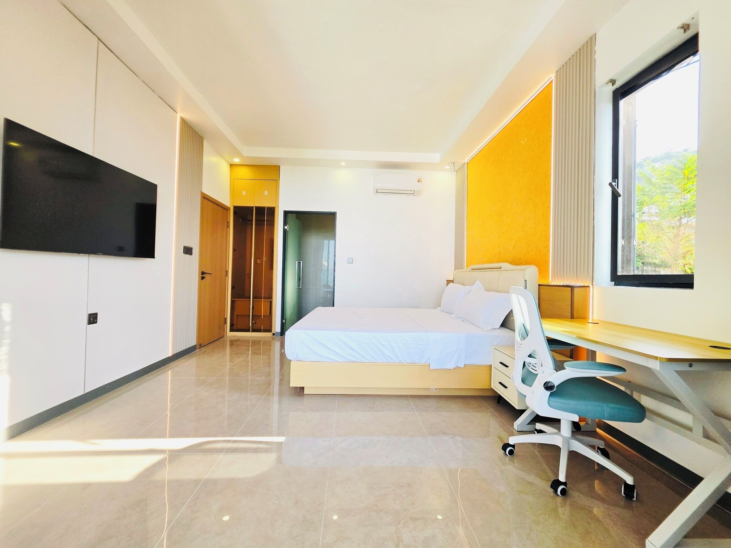 Una habitación de hotel moderna con cama, escritorio, silla y televisor montado en la pared.