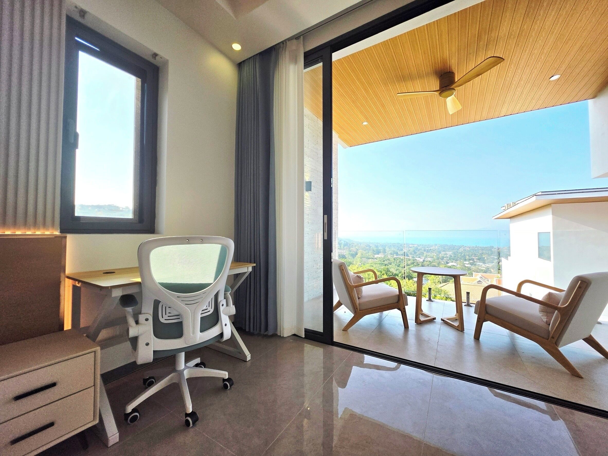 A modern office space with a desk, office chair, and a view of a balcony with chairs.