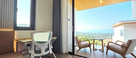 A modern office space with a desk, office chair, and a view of a balcony with chairs.