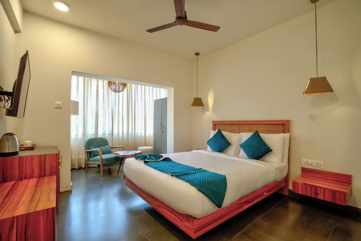 A hotel room with a bed, a desk, a chair, a ceiling fan, and a window with curtains.