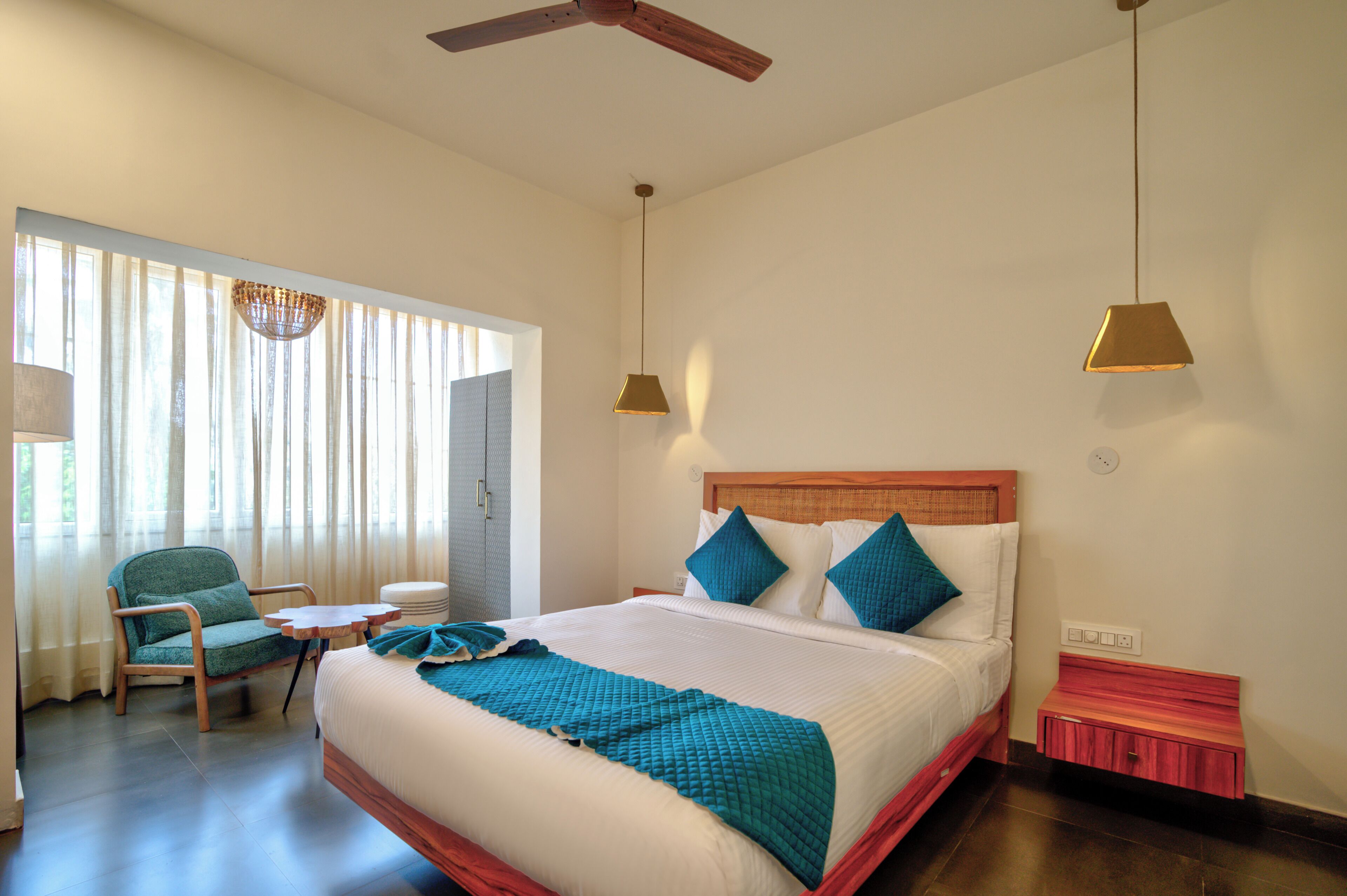 Una habitación de hotel con una cama, una silla, una mesita y un ventilador de techo.