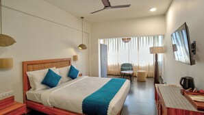 Habitación de hotel con cama, escritorio, silla, ventilador de techo y televisor.