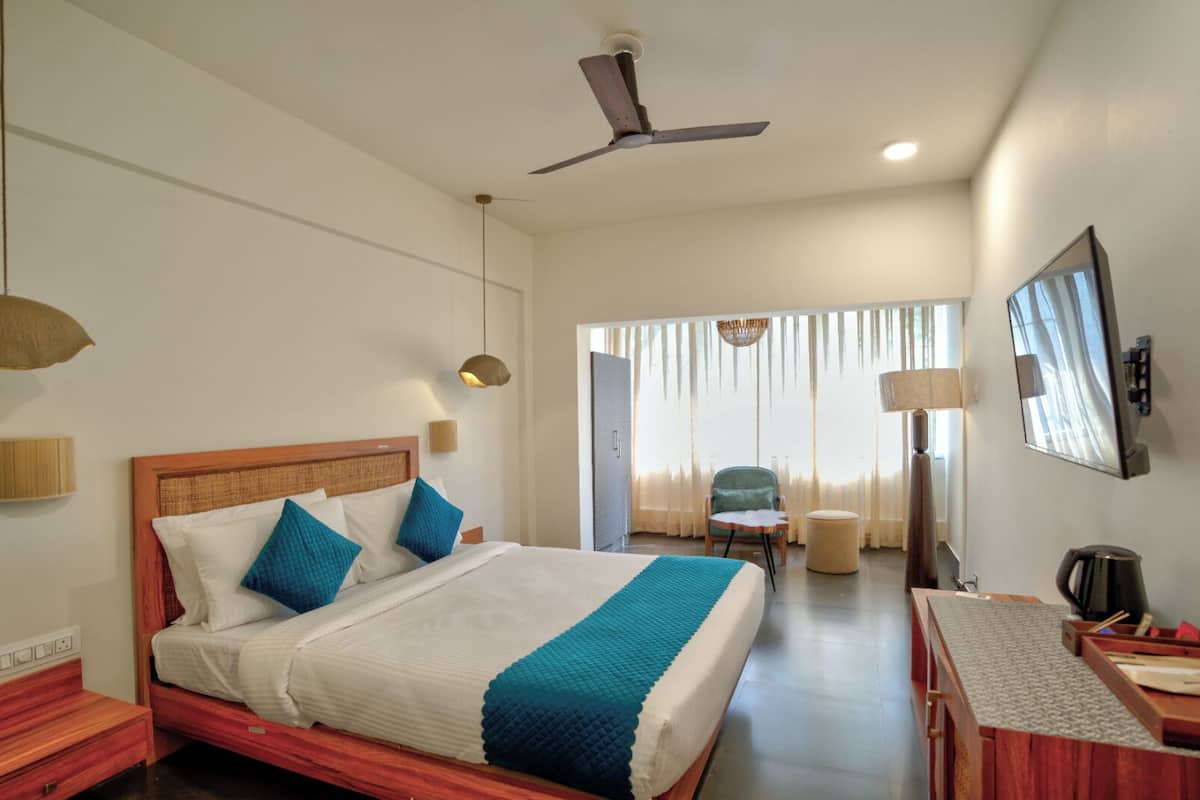 A hotel room with a bed, a desk, a chair, a ceiling fan, and a television.