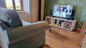 Ett vardagsrum med en grå soffa, en tv-apparat på ett vitt tv-bord och ett trägolv.