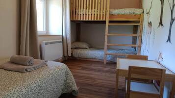 Een kamer met twee bedden, een stapelbed, een tafel, een stoel, een radiator en een raam met gordijnen.