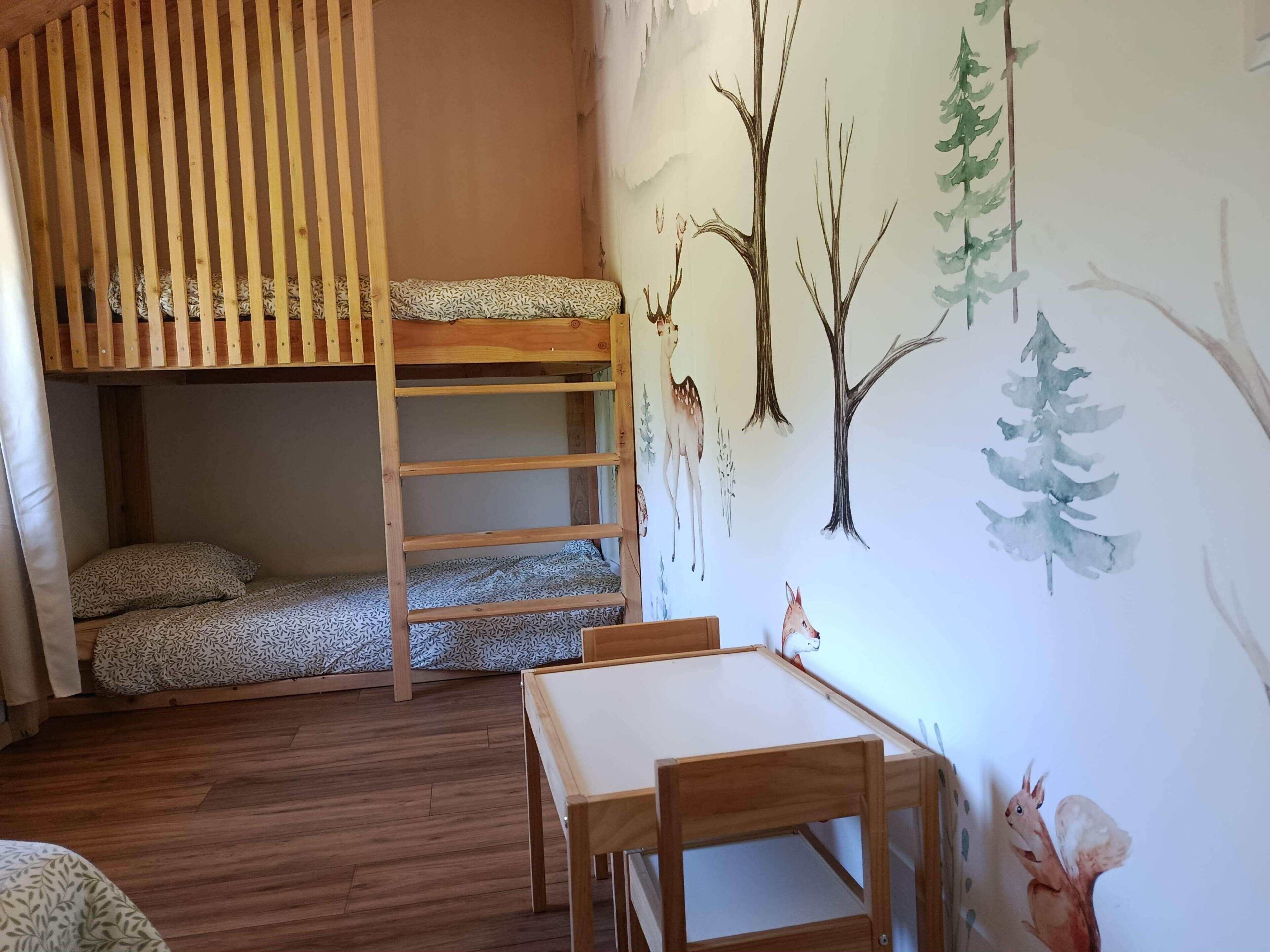 En våningssäng med en stege, ett litet bord och stolar, och en vägg dekorerad med naturbaserad väggkonst.