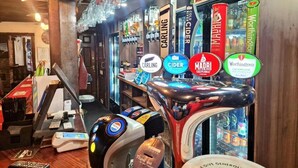 A bar area with multiple taps for different beverages, a cash register, and a menu board.