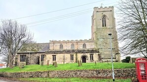 A historic stone church with a tall tower, a red telephone booth, and a grassy area with headstones.