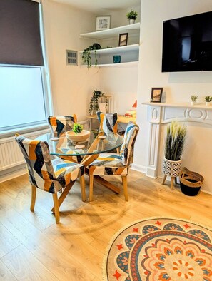 A dining area with a glass table, patterned chairs, a decorative rug, and a fireplace with plants. - Townhouse - 8 Mins from Leeds - Short & Long Stays (Leeds)