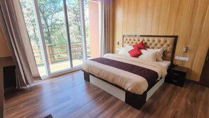 A bedroom with a bed, a nightstand, and a sliding glass door leading to an outdoor area. - Indra Stay by Panache Hotels (Baijnath)
