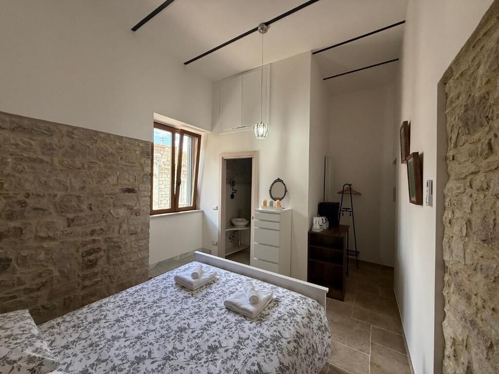 A bedroom with a bed, a window, a wardrobe, and a bathroom visible through an open door.