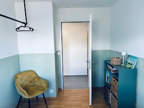 A room with a wooden floor, a yellow chair, a teal bookshelf, and a door leading to another room.