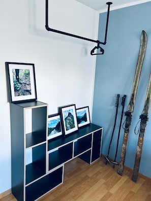 Una habitación con una estantería negra que muestra fotografías enmarcadas, un par de esquíes apoyados contra la pared, y una lámpara colgante.