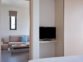 Una habitación de hotel moderna con una cama, un televisor sobre un mueble, un sofá con cojines y una mesita con un arreglo floral.