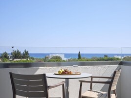 Un balcón con una mesa, dos sillas, una bandeja de fruta y vistas al mar y edificios.