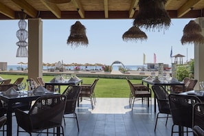 An outdoor dining area with tables and chairs, overlooking a beach and a clear sky. - Atlantica Mikri Poli Rhodes (Rhodes)