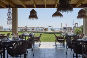 Un espacio de comedor al aire libre con mesas y sillas, con vista a una playa y un cielo despejado.