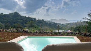 A swimming pool with lounge chairs in the foreground, surrounded by a garden with rocks and plants, and a view of distant hills and mountains. - Villa Ty Kas Soley Sainte Luce, sea view and swimming pool (Sainte-Luce)