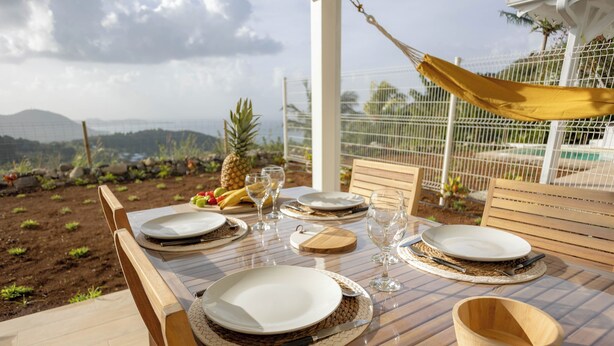 A dining table set outdoors with plates, glasses, and a bowl, surrounded by chairs and a hammock. - Villa Ty Kas Soley Sainte Luce, sea view and swimming pool (Sainte-Luce)