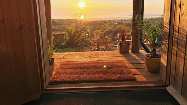 Una puerta de madera que da a un balcón con vistas a la puesta de sol sobre un paisaje.