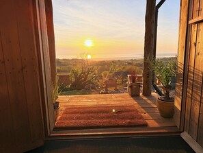 A wooden door leading to a balcony with a view of the sunset over a landscape.