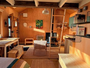 A cozy room with wooden walls, a loft bed, a ladder, a fireplace, and shelves with books.