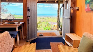 Interior de madera con vista al océano, una puerta que da al exterior y una pequeña mesa con un tazón y tazas.