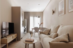 A modern living room with a flat-screen TV, a sofa, a coffee table, and a dining area with chairs and a table.