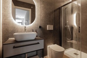 A modern bathroom with a large oval sink, a glass-enclosed shower, and a toilet.