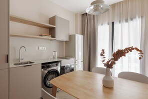 Une cuisine moderne équipée d’un lave-linge intégré, d’une table à manger agrémentée d’un vase et d’une fenêtre ornée de rideaux légers.