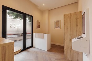 A hotel reception area with a wooden reception desk, a glass door leading outside, and framed pictures on the wall.