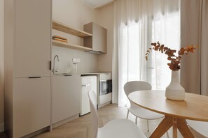 Une cuisine moderne avec des meubles blancs, un four encastré et un coin repas comprenant une table ronde et des chaises.