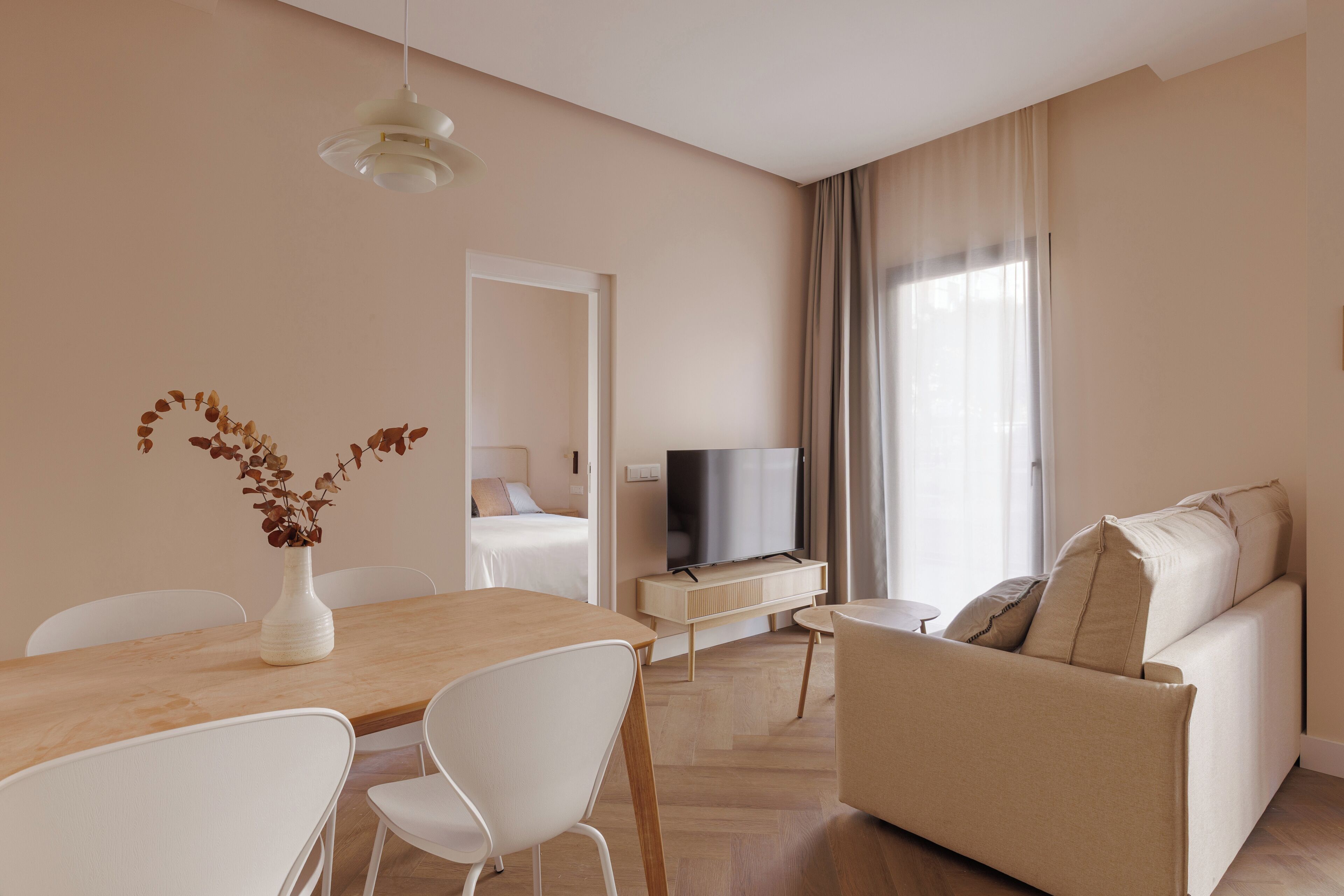 A modern living room with a sofa, a TV, a dining table with chairs, and a vase with dried flowers.