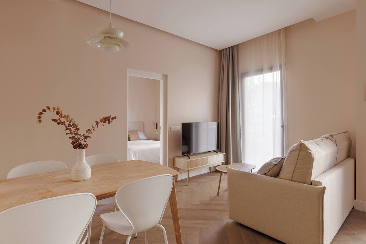Un salon moderne comprenant un canapé, un téléviseur, une table à manger avec des chaises et un vase contenant des fleurs séchées.