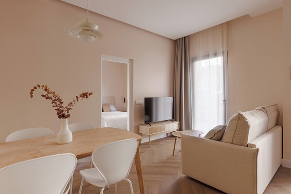 A modern living room with a sofa, a TV, a dining table with chairs, and a vase with dried flowers.