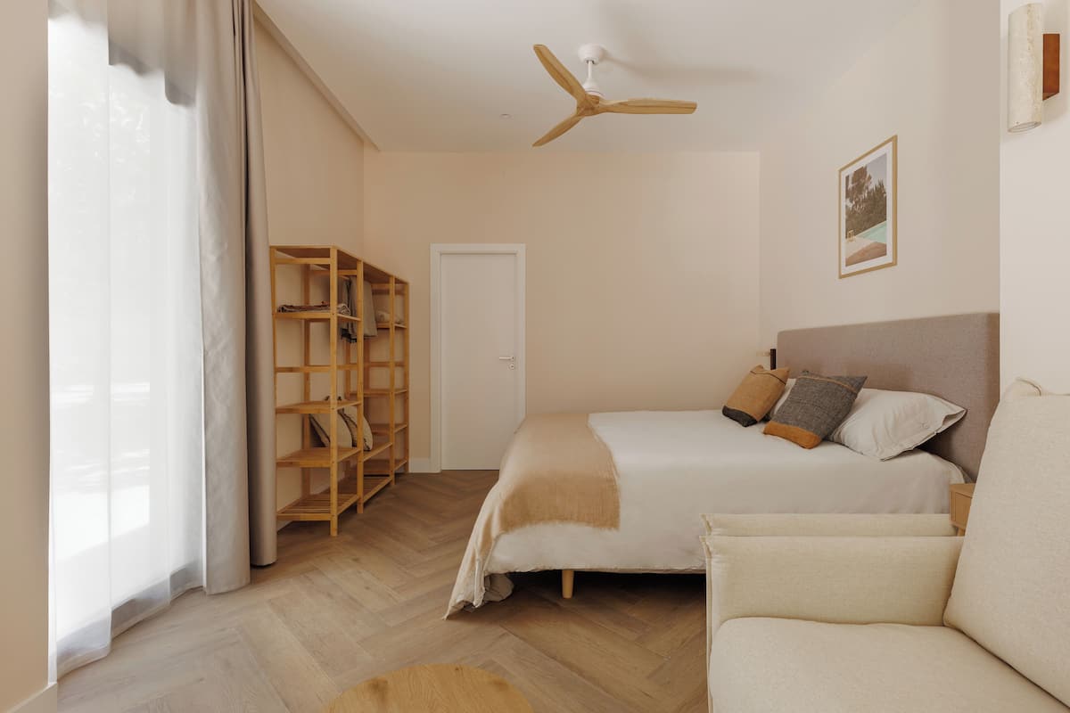Une chambre à coucher avec un lit, une armoire en bois, un ventilateur de plafond et un tableau encadré au mur.