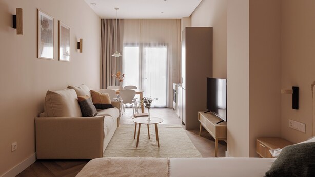 A modern hotel room with a sofa, a small round table, a TV, and a large window. - MH Apartments Blasco Valencia (Valencia)