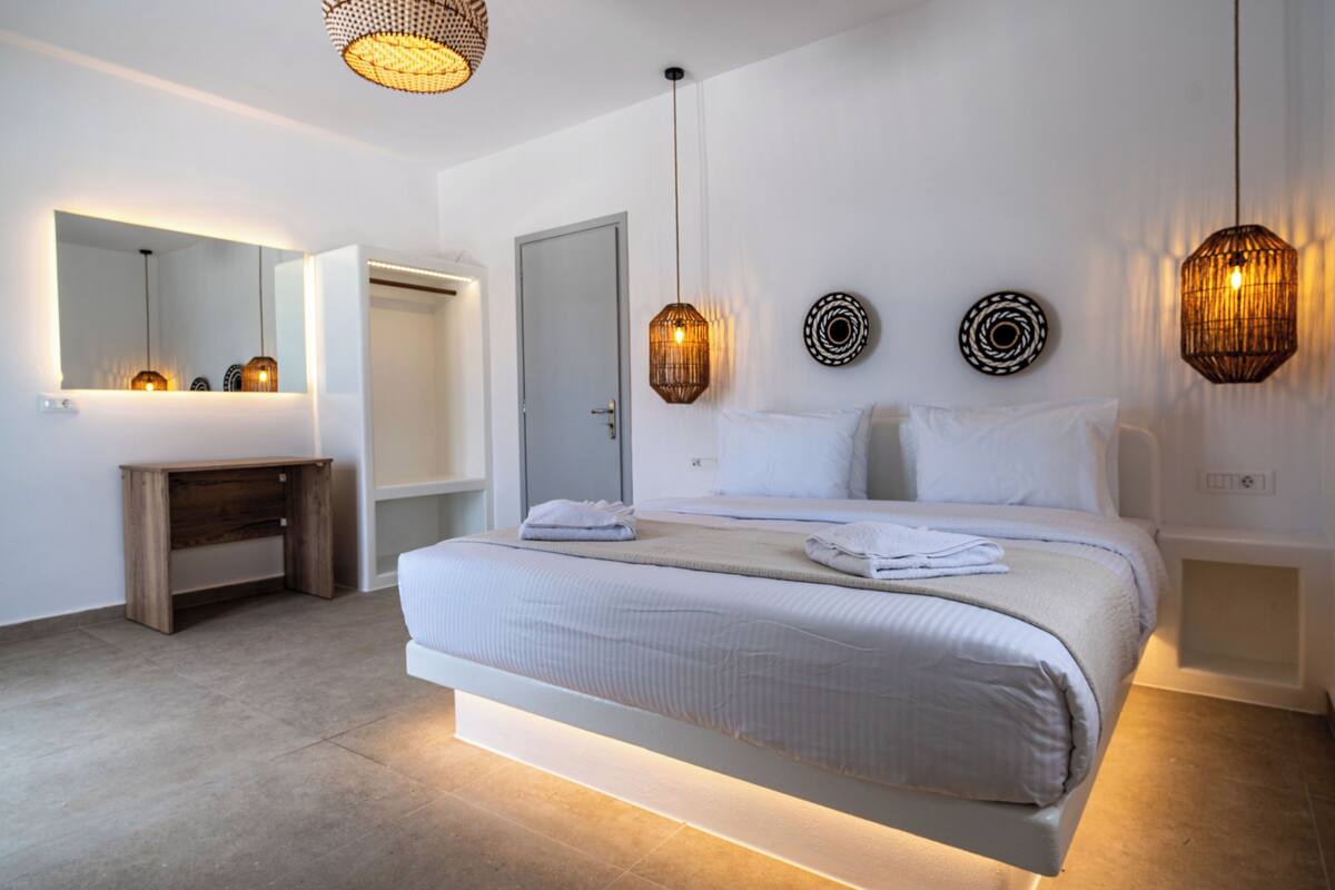 Une chambre moderne avec un grand lit, des tables de chevet, un miroir et des appliques murales décoratives.
