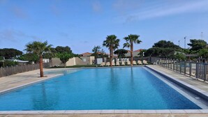 Una piscina rectangular con solárium alicatado, rodeada de palmeras y una valla.