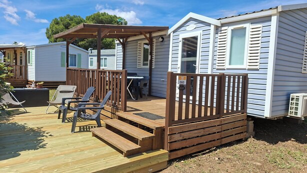 Una casa móvil con terraza de madera, mobiliario exterior y un porche cubierto.