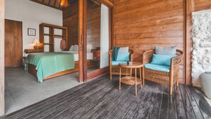 A wooden interior with a bed, a wicker chair, and a small table. - Deluxe Room with Pool Access (Uluwatu)
