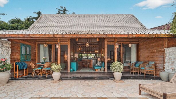 A wooden villa with a tiled roof, a stone patio, a swimming pool, wicker furniture, and a dining area. - Deluxe Room with Pool Access (Uluwatu)