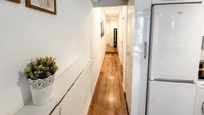 Un pasillo estrecho con suelo de madera, paredes blancas y un refrigerador blanco a la derecha.