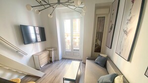 Una sala de estar moderna con un sofá, una mesa de centro, un televisor montado en la pared y una escalera que sube a otro nivel.
