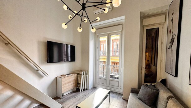 Una sala de estar moderna con una escalera, un televisor de pantalla plana, un sofá y una mesa de comedor.