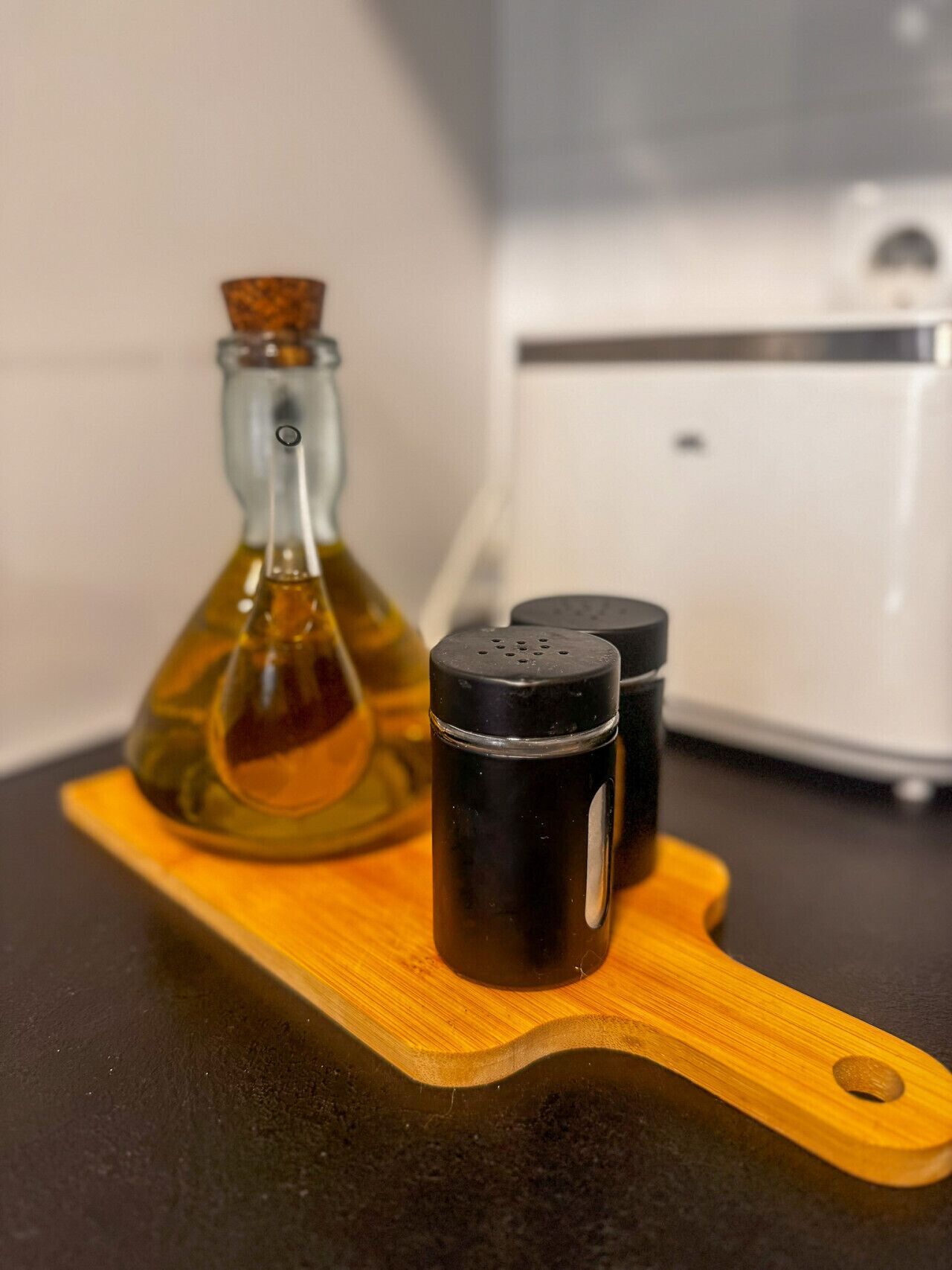 Un piano di lavoro da cucina con un tagliere in legno, una bottiglia di vetro e due dosasali.