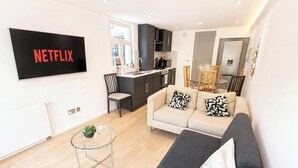 Moderni olohuone, jossa on sohva, sohvapöytä ja televisio, jonka näytöllä näkyy teksti ”NETFLIX”.