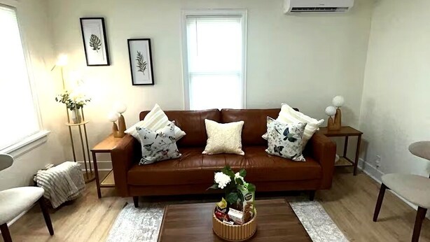 A living room with a brown leather sofa, a coffee table, a patterned rug, and framed artwork on the wall.