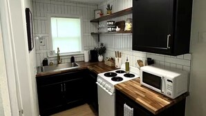A compact kitchen with a stove, microwave, and wooden countertop.